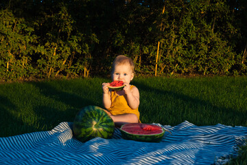 Little kid with watermelon in nature in the garden. Picnic. Summer. Sunset sun.Child eating watermelon in the garden. Kids eat fruit outdoors. Healthy snack for children.