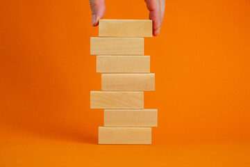 Wall Mural - Concept of building success foundation. Men hand put wooden blocks on the stack of wooden blocks. Beautiful orange background, copy space.