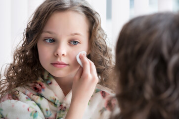 Poster - Portrait of beautiful little girl enjoying skincare cleansing procedures front of the mirror in her home bathroom.