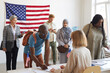 Large multi-ethnic group of people registering at polling station decorated with American flags on election day, copy space