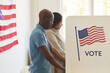 © Seventyfour - Waist up side view portrait of young African-American people standing in voting booth decorated with USA flags, copy space
