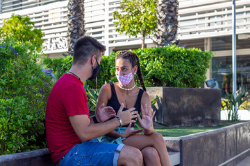 Pareja joven con mascarilla respetando el distanciamiento social en un espacio publico. 