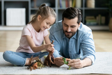 Happy father and little daughter playing with toy dinosaurs close up, sitting on warm floor with underfloor heating, smiling dad and overjoyed girl child enjoying leisure time at home together