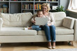 © fizkes - Smiling grandmother and little granddaughter using laptop together, sitting on cozy couch in living room, surfing internet, shopping online, watching video or cartoons, having fun on weekend