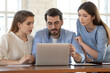 © fizkes - Businesswoman realtor consulting young couple at meeting, using laptop, pointing finger at screen, demonstrating presentation, man and woman discussing mortgage or loan conditions with manager