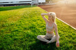 © Maria - Beautiful young blonde woman in sportswear sits on the grass in the stadium before training