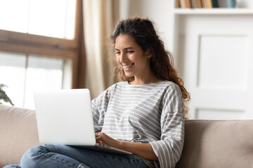 Woman smile sit on couch put pc on laps involved in webinar distant activity, do remote job, have fun on internet, read pleasant news, message from friend, shopper make purchase buying on-line concept