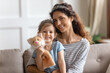 Little daughter hold hand puppet cat fluffy toy sit on mother laps, girls wear crowns smile look at camera. Happy family single mom her kid girl portrait, developing games, having fun playtime concept