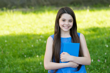 Little smart girl with book outdoors sunny day, self education concept