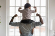 Back side view young african american father holding on shoulders little preschool funny kid son, showing biceps. Fit strong different generations family enjoying domestic activity, healthcare concept