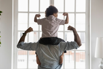 back side view young african american father holding on shoulders little preschool funny kid son, sh