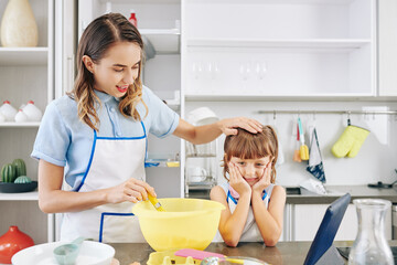 Wall Mural - Cooking mother stroking head of daughter waiting for cake to be done