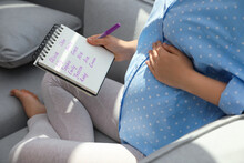 Pregnant Woman With Baby Names List Sitting On Sofa, Closeup