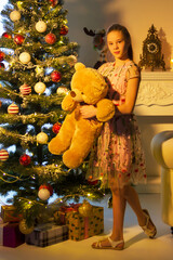 Wall Mural - Teenage Girl Standing near Christmas Tree Holding Big Teddy Bear