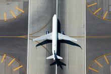Aerial View Of Narrow Body Aircraft Departing Airport Runway. Top Down View Of White Unidentified Airplane In The Center Of Taxiway Lines. Aviation Industry.