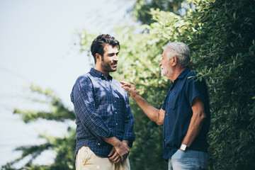 The happy elderly father and son spent time togerther with smiliing, laughing and talking at cozy home garden. Concept of freindly family