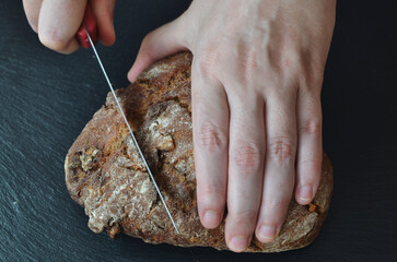 Manos de una persona cortando un pan artesano de nueces sobre un plato de pizarra