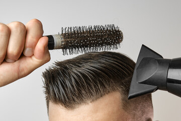 Man styling his hair with hair dryer and round brush. Hair care at home after barbershop. Mans fashion and modern haircut.