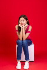 Wall Mural - Portrait pretty young asian woman. Lovely girl sitting on a chair. She wear jeans, snickers shoe. Cute female is good looking girl, she has nice smile. red background, copy space, taken full length