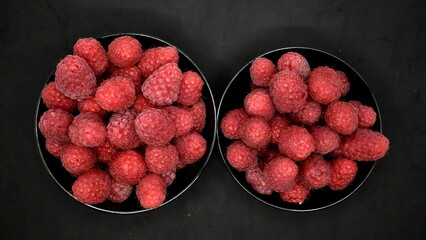 Red raspberries in two black cups on a black background.
Red natural and fresh raspberries. Black background