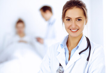 Wall Mural - Female doctor smiling on the background with patient in the bed and two doctors