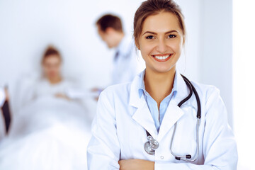 Female doctor smiling on the background with patient in the bed and two doctors