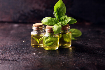 Wall Mural - A transparent glass bottle of basil essential oil with fresh basil leaves on rustic table