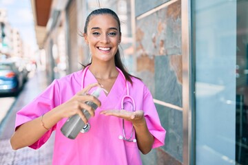 Wall Mural - Young hispanic doctor woman using hand sanitizer gel at street of city.