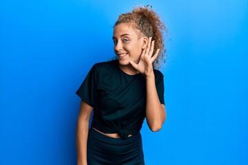 Beautiful caucasian teenager girl wearing black sportswear smiling with hand over ear listening an hearing to rumor or gossip. deafness concept.