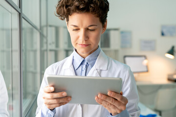 Wall Mural - Young serious scientist or chemist in whitecoat looking through information