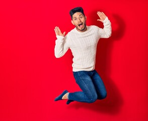 Young handsome latin man wearing casual clothes smiling happy. Jumping with smile on face over isolated red background