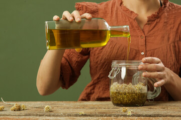 Woman making herbal infused oil with yellow immortelle flowers. Process of maceration for natural organic cosmetic.