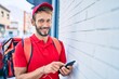 © Krakenimages.com - Caucasian delivery man wearing red uniform and delivery backpack smilly happy outdoors using smartphone