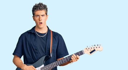 Young handsome man playing electric guitar scared and amazed with open mouth for surprise, disbelief face