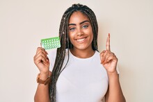 Young African American Woman With Braids Holding Birth Control Pills Surprised With An Idea Or Question Pointing Finger With Happy Face, Number One
