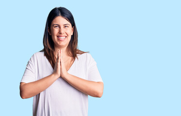 Young beautiful brunette woman wearing casual t-shirt praying with hands together asking for forgiveness smiling confident.