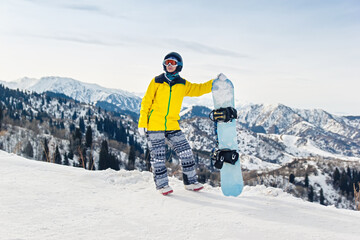 Young woman snowboarder in a yellow jacket and black helmet on the background of snowy mountains