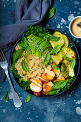 Canvas Print - Vegan lunch plate. Quinoa salad with baked zucchini, sweet potato, avocado and tahini dressing in black plate, dark background, top view.