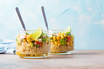 Vegan salad with vegetables and quinoa in glass jars, blue background.