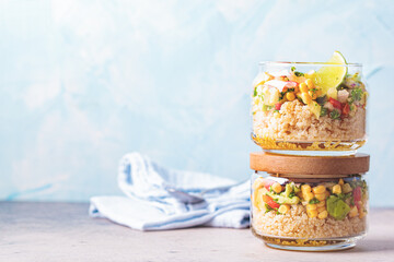 Vegan salad with vegetables and quinoa in glass jars, blue background.