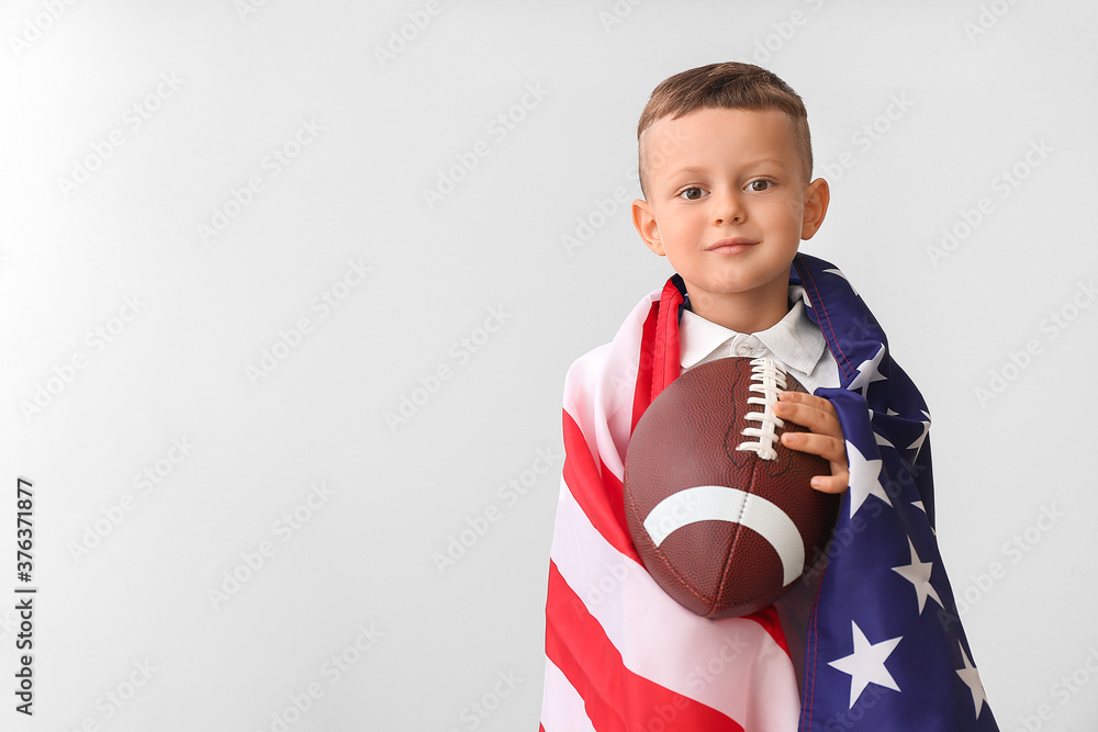 Little boy with rugby ball and USA flag on light background