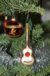 Weihnachtsdekoration auf dem Tannenbaum. Eine rote Glaskugel mit goldene und grüne Motive und eine Glas Gitarre mit rot, weiß und gold, silberne Lametta hängen an die grüne Tannenzweige.