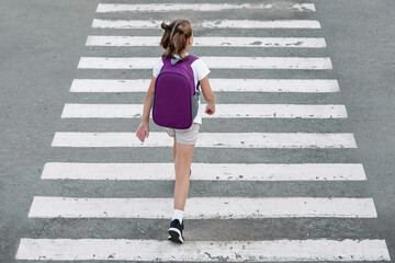 Schoolgirl crossing road on way to school. Zebra traffic walk way in the city. Concept pedestrians passing a crosswalk.  Stylish young teen girl walking with backpack. Active child. Top view