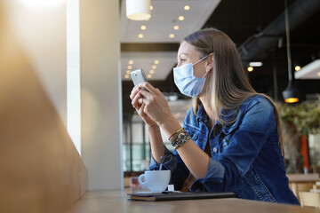 Wall Mural - Young woman sitting at coffee shop and working on laptop with face mask