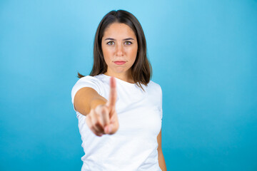 Young beautiful woman over isolated blue background showing and pointing up with fingers number one while is serious