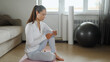 © lenblr - pretty girl with ponytail in sportswear looks for new training manual on mat surfing internet with smartphone on floor at sofa in room