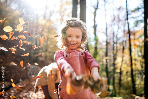 Fotografía Small girl with mother on a walk in autumn forest, throwing leaves