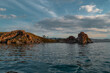 © SymbiosisArtmedia - Red cape Shamanka in clear blue Lake Baikal among the rocks, mountains and clouds, sunset, ripples