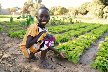 food for africa! young black boy smiling in front of lettuce salad field