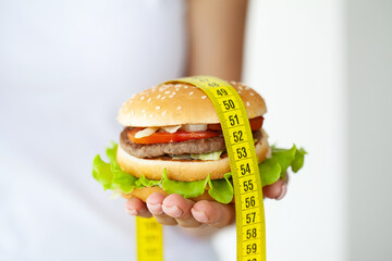 Diet concept, woman holding harmful fat burger with yellow measuring tape